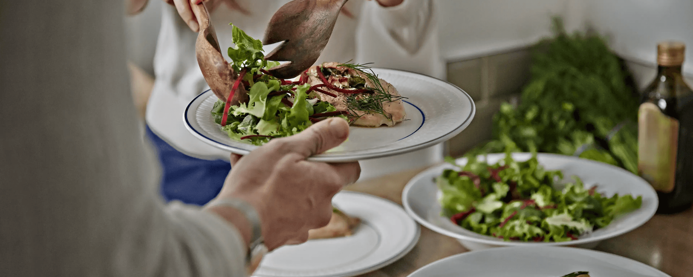 Person using utensils to put salad on a plate.